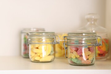 Tasty gummy candies in jars on shelf, closeup