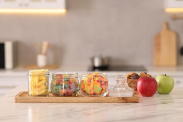 Tasty gummy candies, apples and cookies on white marble table