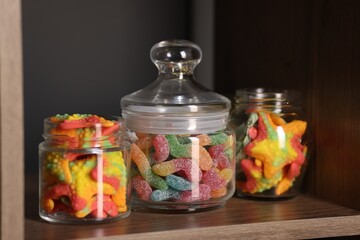 Tasty gummy candies in jars on shelf, closeup