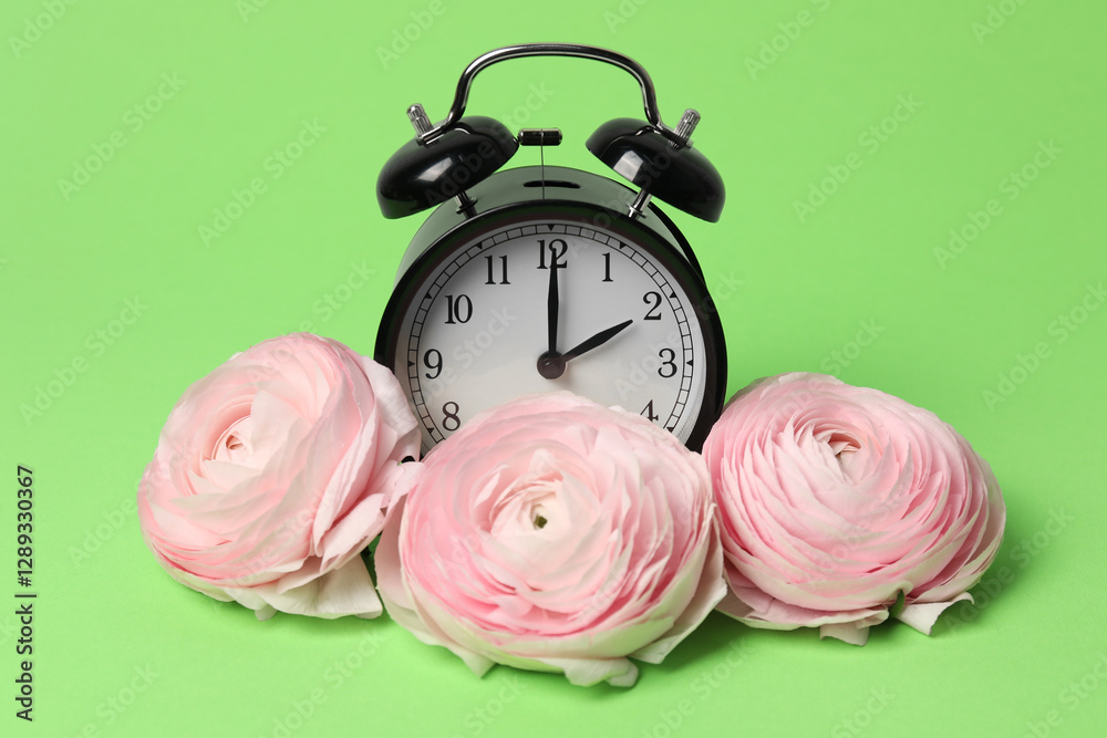 Poster spring time. alarm clock and beautiful ranunculus flowers on green background
