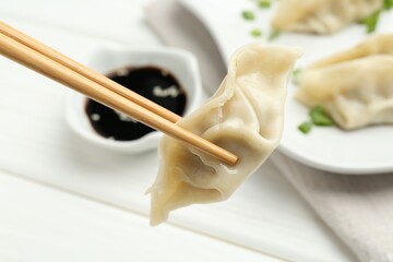Chopsticks with tasty boiled gyoza (dumpling) over white table, closeup