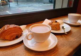 Cup of hot chocolate, cup of coffee with a pain au chocolat, chocolatine, viennoiseries, pastries and scone for a cosy and comfy coffee shop and bakery design background