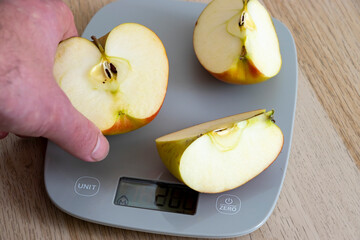 Hand holding a sliced apple on a digital scale, showcasing healthy eating and nutrition. Fresh fruit is ideal for diet-related content.