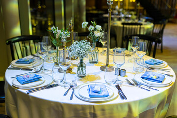 Wedding table setting with plates, blue napkins, wine glasses, and bouquets of lisianthus and...