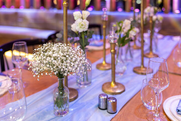 bar mitzvah  table setting with plates, blue napkins, wine glasses, and bouquets of lisianthus and gypsophila, along with kerosene lamps for a wedding event.