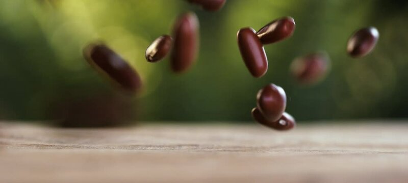 Close-up view of red azuki beans falling on wooden surface in slow-motion. Raw uncooked Adzuki grains