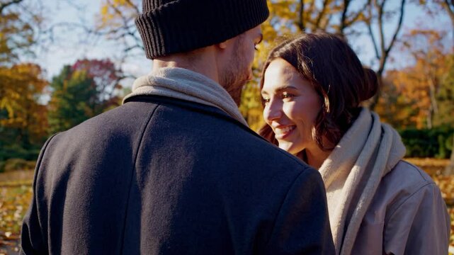 A couple walks through a park in autumn, captured from a low-angle shot. The video style highlights vibrant fall foliage and a serene atmosphere.