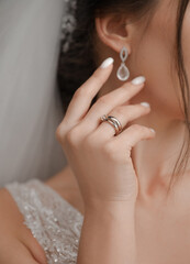 A close-up of a woman’s ear and hand with a delicate natural manicure and an elegant gemstone ring. Soft pastel tones and free space for text perfect for beauty and jewelry themes.