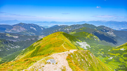 Hikers enjoy stunning panoramic views from a trail in Low Tatras National Park, surrounded by lush greenery and distant mountain ranges under a clear blue sky. © pyty