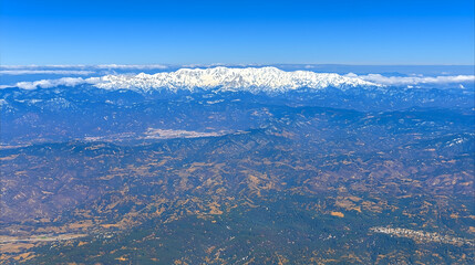 Naklejka premium Aerial view of snow-capped mountain range above valley, seen from airplane window, used for travel brochures