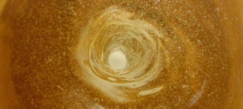 Macro cinematic shot of fresh beer rotating inside the glass bottle at the bar