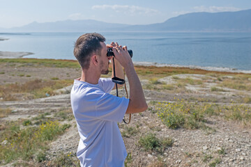 Young man birdwatching with a telescope by a lake.