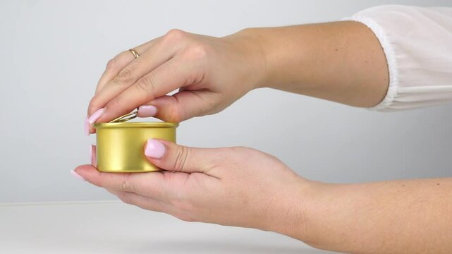 Woman opening gold tin can with safe pull tab in hands against white background