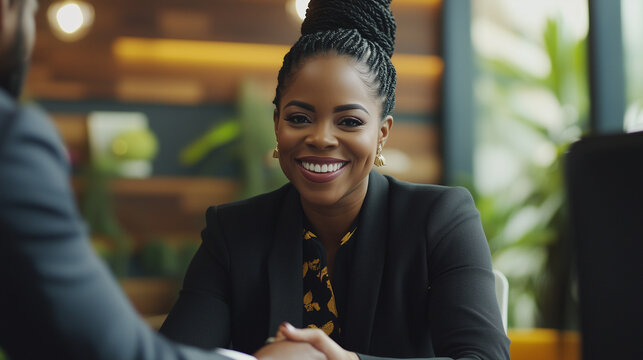 A professional Black woman shaking hands with a colleague in a modern open-concept office - Powered by Adobe