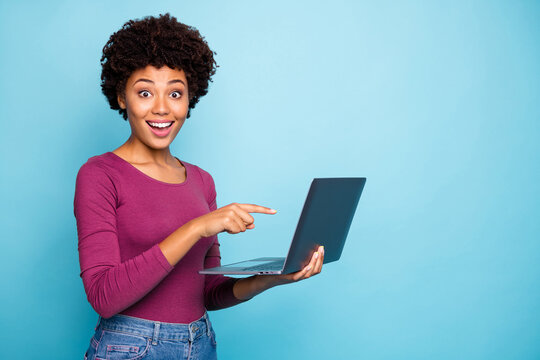 Photo of cute stylish trendy black model pointing at laptop recommending you to purchase it requesting to follow on social media wearing hreen sweater jeans denim isolated vivid color blue background