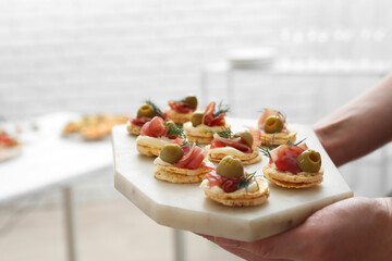 Woman holding board with tasty canapes indoors, closeup