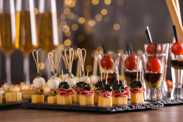 Many different tasty canapes and wine on wooden table against blurred lights