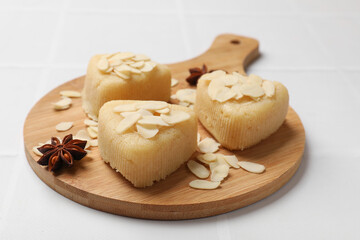 Pieces of delicious sweet semolina halva with almond flakes on white tiled table, closeup