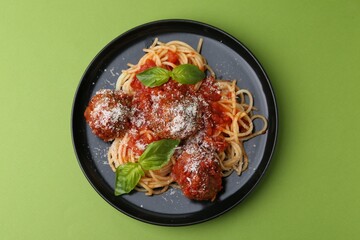 Delicious pasta with meatballs, basil and cheese on green table, top view