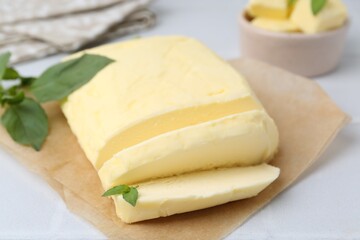 Cut brick of butter and basil on white table, closeup