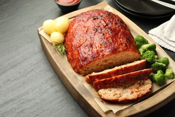 Delicious turkey meatloaf with vegetables served on black table, closeup