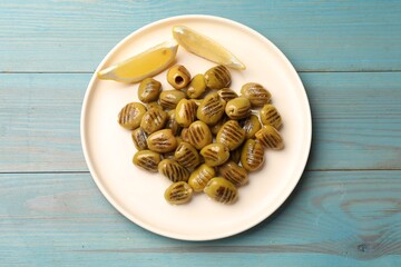 Grilled green olives and lemon wedges on light blue wooden table, top view