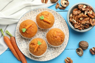 Tasty carrot muffins, walnuts and fresh vegetables on light blue wooden table, flat lay