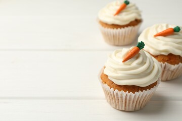 Tasty carrot muffins with cream on white wooden table, closeup. Space for text