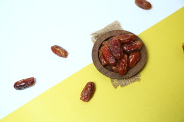 Delicious dates in a wooden plate with yellow and white backgroud