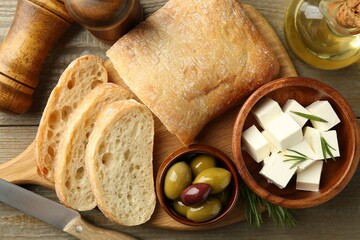 Delicious marinated olives, bread and feta cheese served on wooden table, flat lay