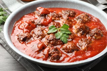 Delicious meatballs with tomato sauce in frying pan on table, closeup