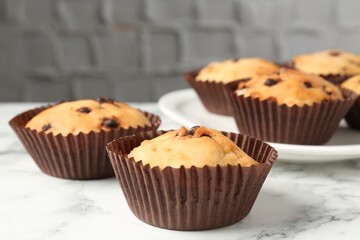 Delicious muffin with chocolate chips on white marble table, closeup