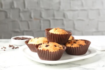 Delicious muffin with chocolate chips on white marble table, closeup