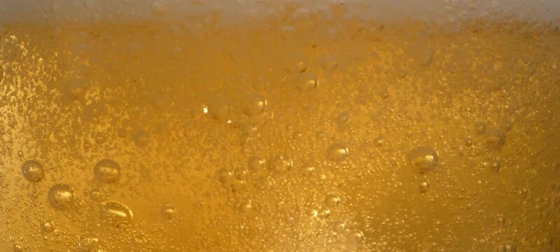 Extreme close-up view of craft beer bubbles floating to the top of a pint glass in slow-motion