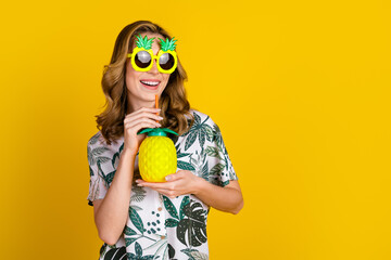 Cheerful Woman Wearing Pineapple Sunglasses Holding a Tropical Drink Against a Bright Yellow Background