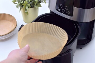 A woman places a paper disposable liner into a deep fryer.Paper for air fryer