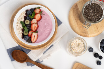 Presented by fruits putting yogurt toppings with strawberry, berry, oats, raisins and chia seed decorated by peppermint in white blow. Pink background. Set of healthy dairy product choice. Pecuniary.