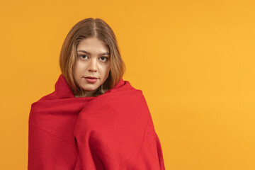 A woman wrapped in a red shawl, with a neutral expression, against a yellow background