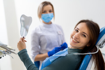 Patient smiles at dental checkup. A young woman smiles while holding a dental mirror at a clinic. A hygienist prepares for a routine examination.
