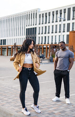 Obraz premium City folks basking in sunlight. Two individuals engage in a casual outdoor moment, with one walking and the other watching under clear skies.
