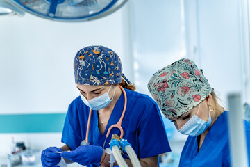 Health pros focus on care. Two healthcare workers in scrubs and masks are focused on a task in a...