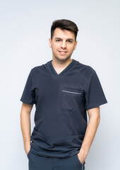 Confident young male doctor. A male healthcare worker in scrubs stands with a friendly smile against a plain background.