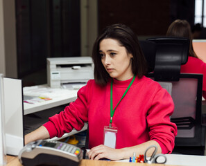 Dedicated woman in office. A woman in a red sweater concentrates on her work at a desk with office equipment and supplies around her.