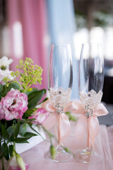 Floral wedding champagne flutes. Glasses decorated with lace and ribbons sit near a floral arrangement, creating a beautiful setting for a celebration.