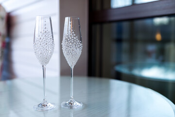 Elegant champagne flutes on a table. Two stylish champagne flutes with decorative patterns sit on a glass table near a large window, reflecting light.