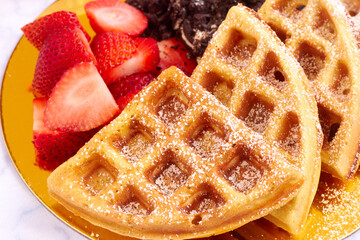 Waffles with powdered sugar served with strawberries and chocolate cookies on golden plate