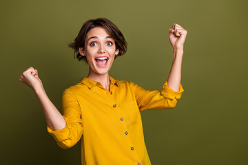 Excited young woman celebrating success with joyful expression wearing yellow shirt on green background