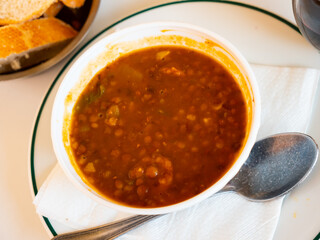 Spicy stewed lentils with suasage and vegetables with thick tomato sauce served in white plate. Typical Spanish cuisine