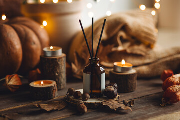Cozy interior with knitted sweater, burning candles and aroma perfume stick diffuser in a living room. Fall scent, pumpkin. Home comfort, coziness, aromatherapy. Idea for simple atmospheric setting