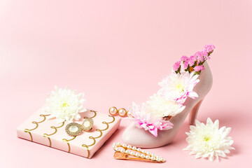 Elegant pink high-heeled shoe filled with fresh flowers. Jewelry, hair accessories, and a wrapped...